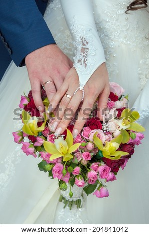 A newly wed couple place their hands on a wedding bouquet showing off their wedding bands.