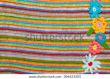 Beautiful, rainbow knitted crochet striped background with flowers. Knitted texture.
