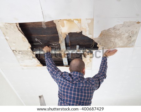 Man repairing collapsed ceiling. Ceiling panels damaged  huge hole in roof from rainwater leakage.Water damaged ceiling .