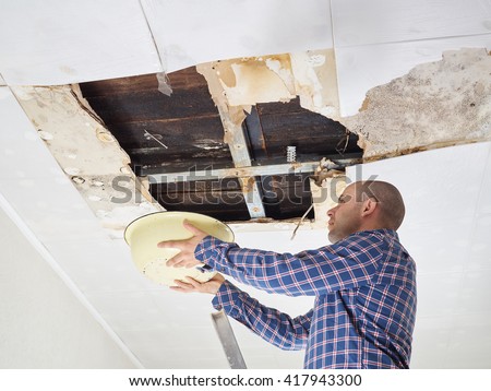 Man Collecting Water In basin From Ceiling. Ceiling panels damaged  huge hole in roof from rainwater leakage.Water damaged ceiling .