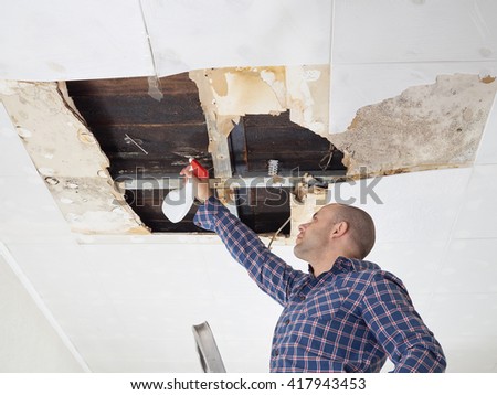 man cleaning mold on ceiling.Ceiling panels damaged  huge hole in roof from rainwater leakage.Water damaged ceiling .