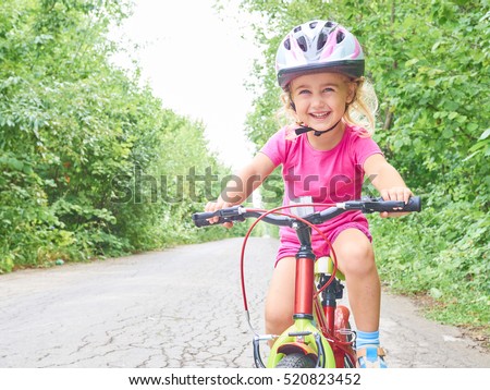 Happy child riding a bike in outdoor. Cute kid in safety helmet biking outdoors. Little girl on a red  bicycle  Healthy preschool children summer activity.