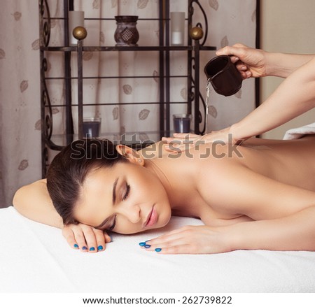 Adult woman in spa salon having body relaxing massage, lying on table, with olive