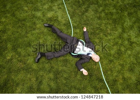 Businessman lying on lawn bounded with garden hose