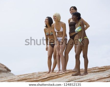 Four female friends in bikinis standing on cliff looking away
