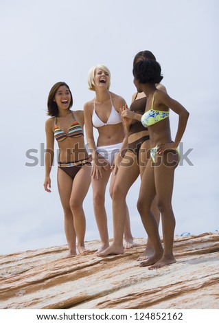 Four female friends in bikinis standing on cliff and laughing