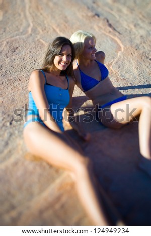 Two female friends sitting in bikinis on cliff
