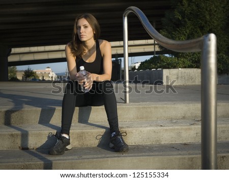 Female jogger sitting on steps with a bottle of water