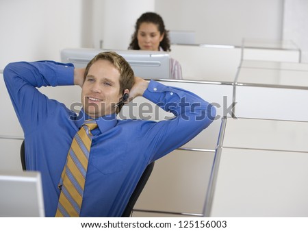 Businessman in cubicle with headset arms up