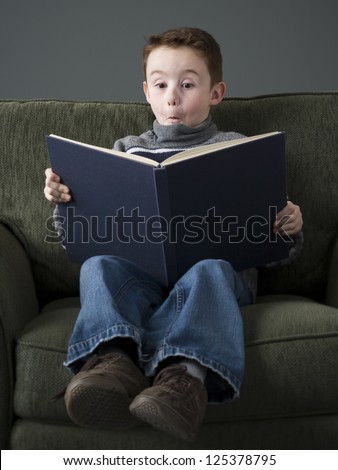 Surprised boy sitting on couch reading a book