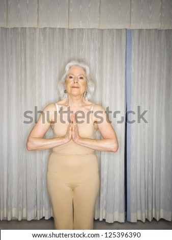 Three quarter length of a senior woman standing with yoga gesture