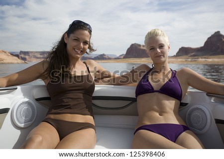 Two smiling women lying on on boat in bikinis