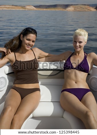 Two young smiling women on boat in bikinis smiling
