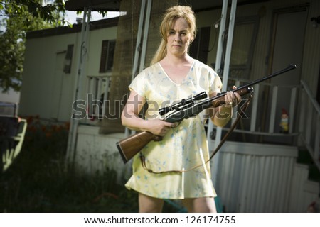 Woman standing in trailer park with rifle