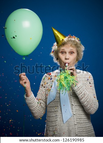 Portrait of older woman with noisemaker, balloon and party hat