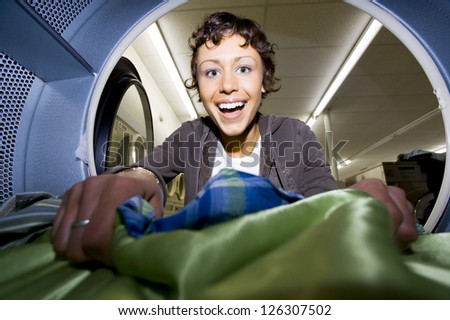 Woman looking into dryer at laundromat with clothing