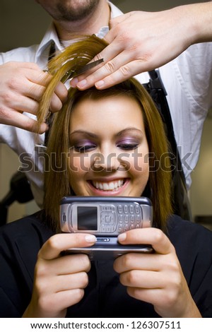 Teenage girl with cell phone having hair cut