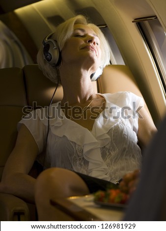 A middle-aged woman wearing headphones and sleeping in an airplane