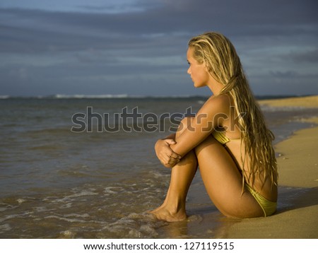 Profile of a teenage girl sitting on the beach and hugging her knees