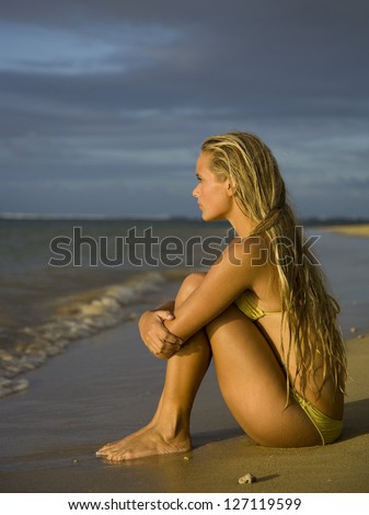 Profile of a teenage girl sitting on the beach with hugging her knees