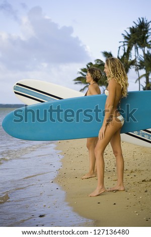 Profile of two young women holding surfboards and standing on the beach