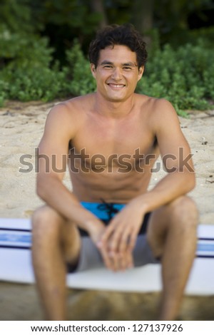 Portrait of a young man sitting on a surfboard and smiling