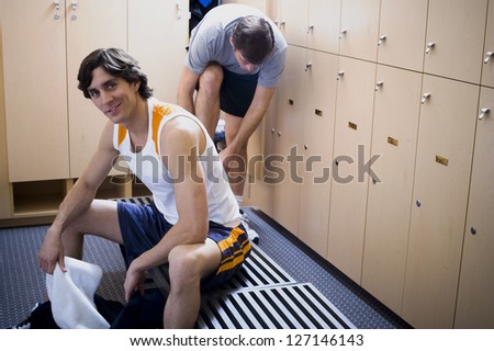 Young man sitting on a bench with a mid adult man tying his shoelaces behind him