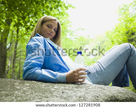 Portrait of a young woman lying on a rock and holding a water bottle