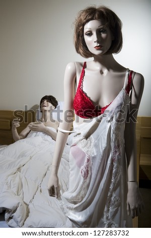 Close-up of a female mannequin half dressed with a male mannequin laughing on the bed behind