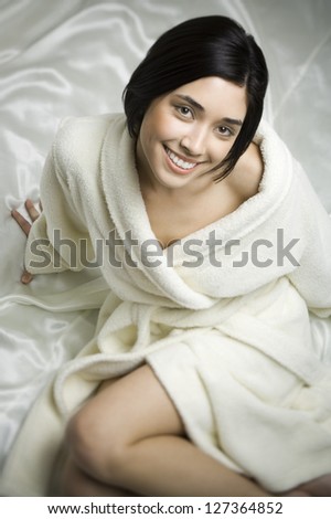 Woman in bathrobe sitting on bed covered with silk bed sheet