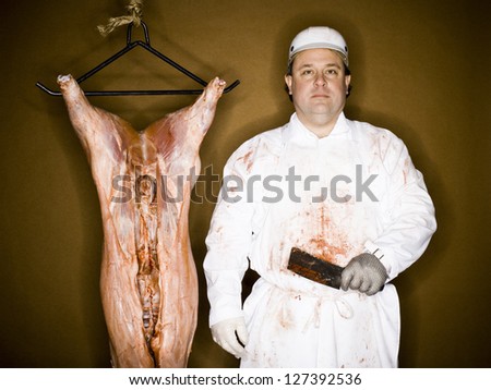 Half length of a butcher with hanging carcass and knife over brown background