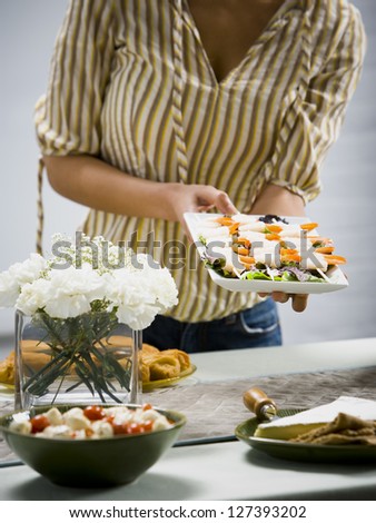 Woman holding tray of sushi with other foods and flower arrangement