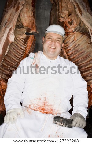 Butcher sitting with carcass and knife while smiling