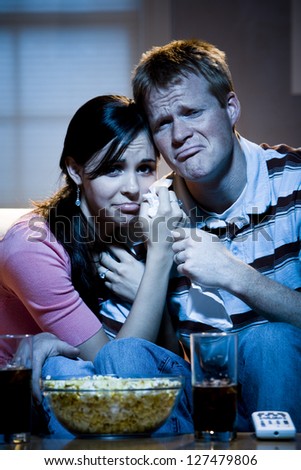 Couple watching television with bowl of popcorn and crying
