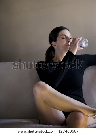 Woman sitting on sofa in black sweater drinking bottled water