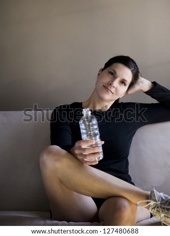 Woman sitting on sofa with bottled water and smiling in black sweater