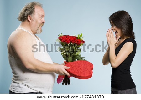 Disheveled man with heart box and red roses with excited woman over gray background