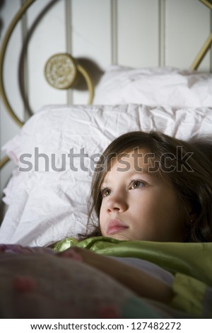 Preteen girl lying in bed covered by blanket