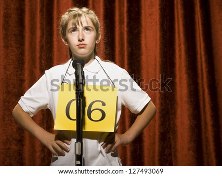 Girl standing at microphone and thinking with hands on hips