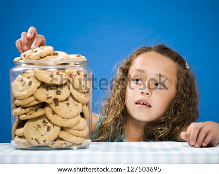 Girl taking chocolate chip cookie from jar