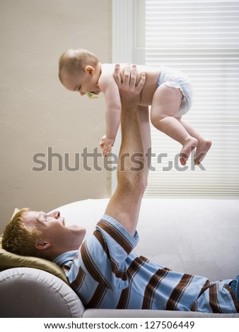 Man lying down on sofa holding baby in air
