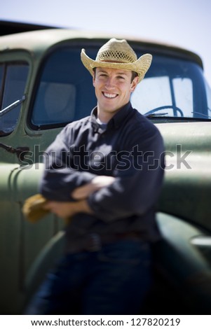 Man in cowboy hat leaning on truck smiling