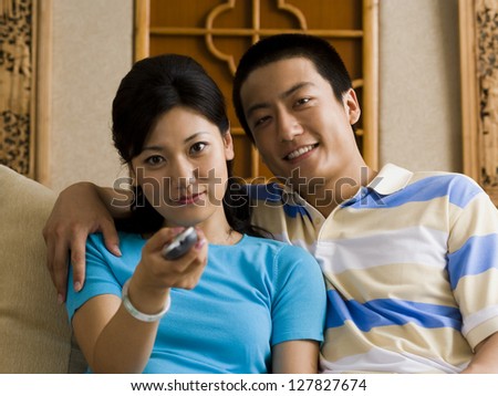 Couple embracing on sofa while woman changes channels with television remote