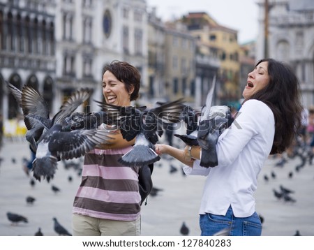 Two women in public square with pigeons laughing