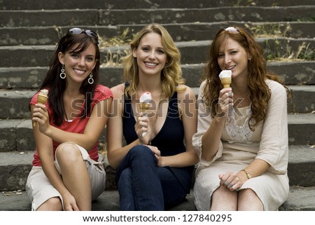 Three women sitting on steps outdoors eating ice cream cones smiling