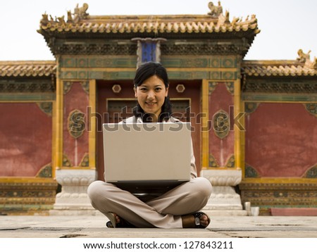 Businesswoman sitting cross legged outdoors with laptop