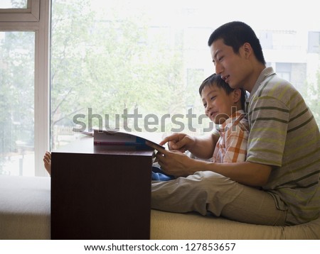 Man and boy sitting and reading in front of large window