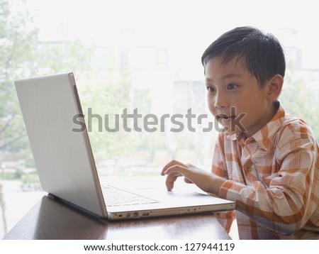 Boy sitting with laptop in front of large window smiling