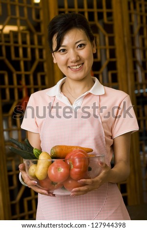 Woman in apron holding bowl of vegetables smiling