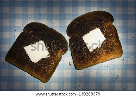 Two pieces of burned toasts with butter on the table